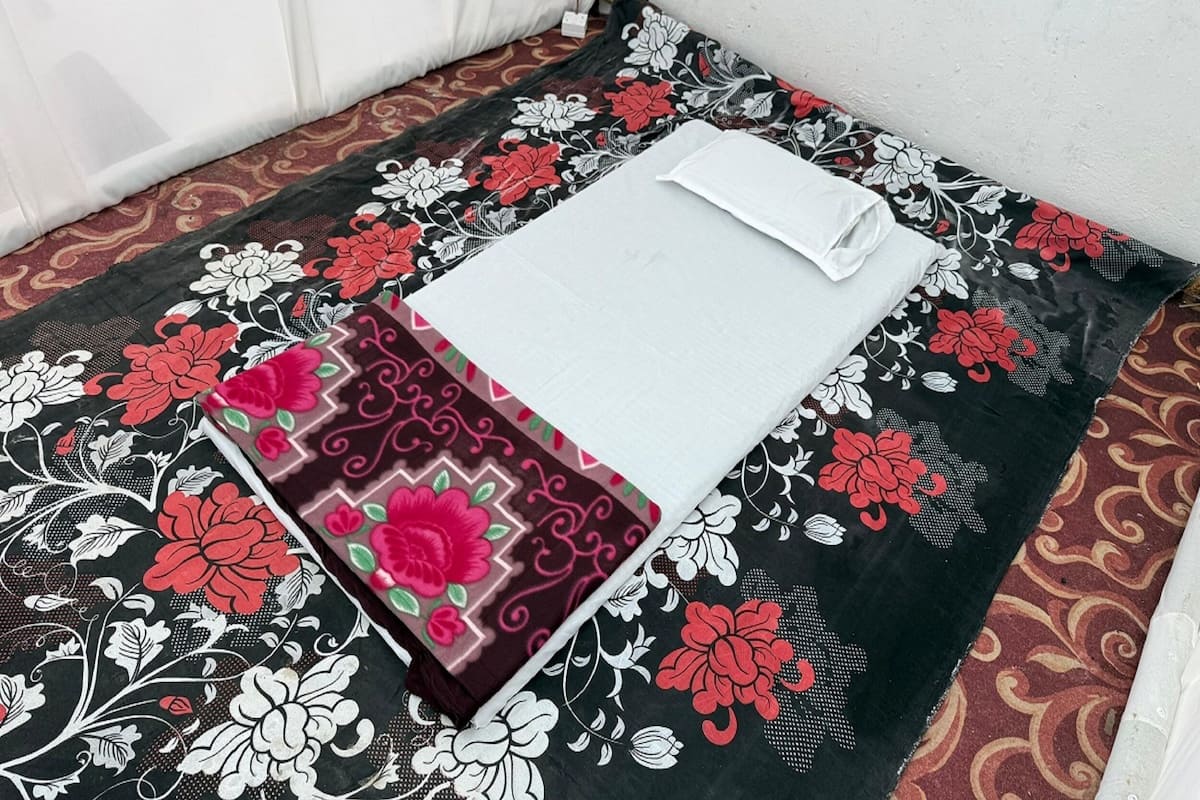 A neatly made bed with a white pillow and a black and red floral bedspread.