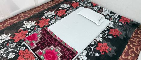 A neatly made bed with a white pillow and a black and red floral bedspread.