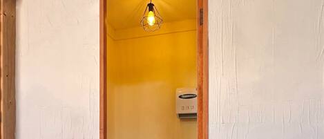 A narrow doorway leading to a bathroom with a toilet, a sink, and a handheld toilet brush. There is a potted plant in the foreground.
