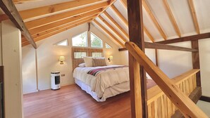 A bedroom with a sloped ceiling, wooden beams, a bed with a striped blanket, two wall-mounted lamps, and a window with curtains. - Rusti.Ko Experiencias (Vicuña)