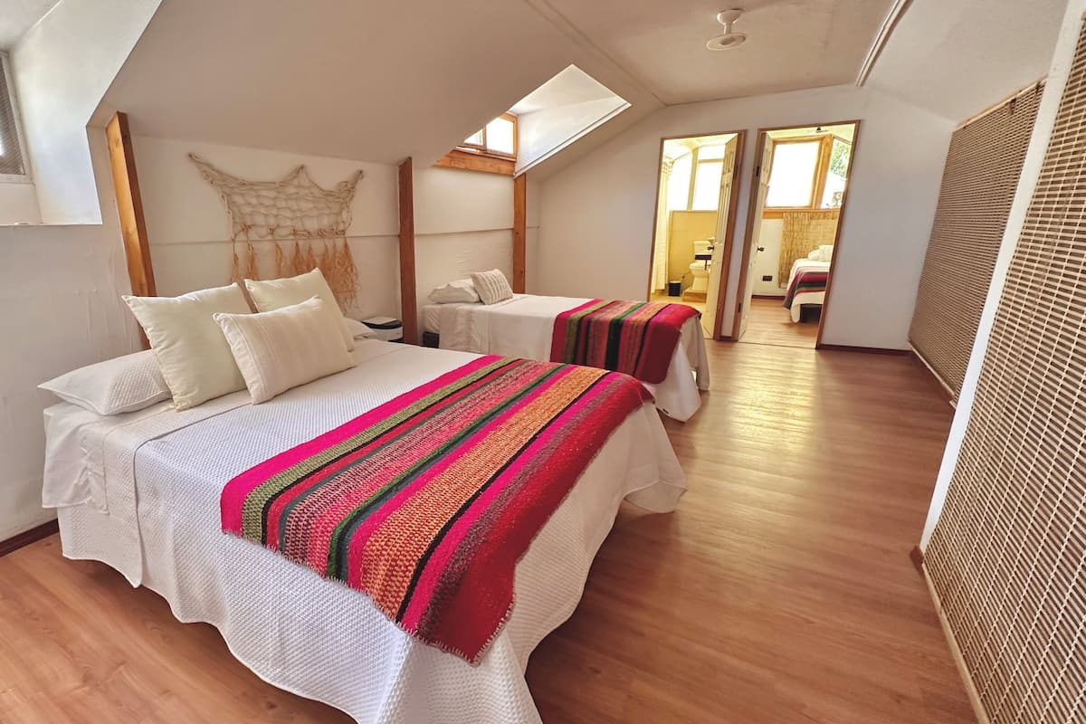 A bedroom with two beds, a skylight, wooden flooring, and a large woven tapestry on the wall.
