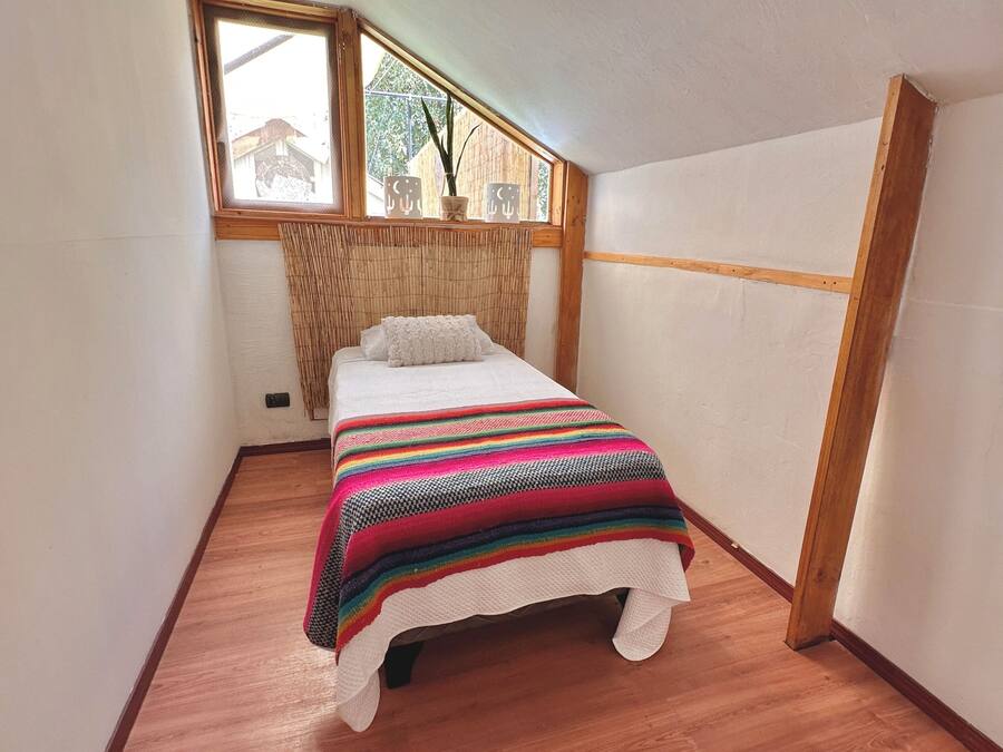 Una habitación pequeña y estrecha con una cama individual, una ventana que da a una casa y una cortina de bambú.