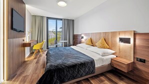 Een moderne hotelkamer met een groot bed, een bureau met stoel, een flatscreen televisie en een balkon met uitzicht.