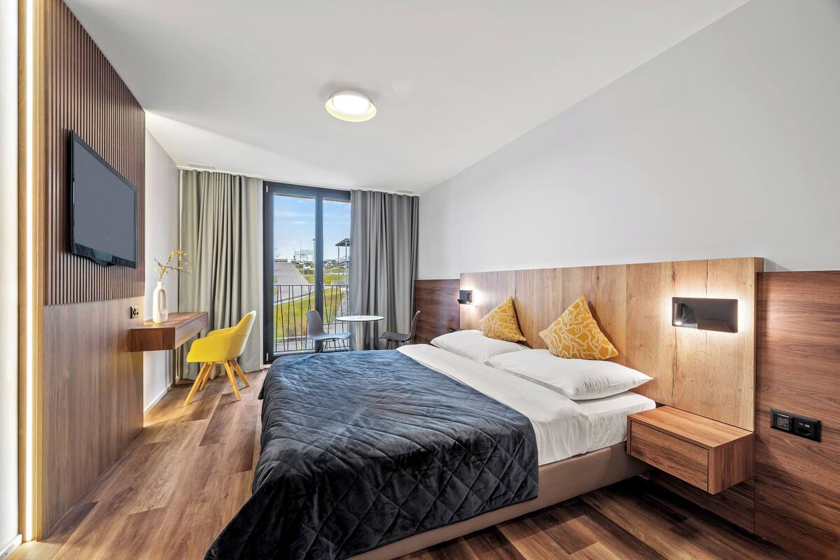 Habitación de hotel moderna con una cama grande, un escritorio con silla, un televisor de pantalla plana y un balcón con vistas.