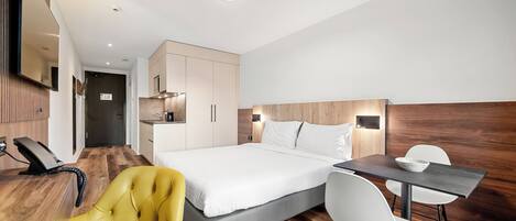 A modern hotel room with a bed, a desk, a chair, a telephone, and a wooden panel wall.