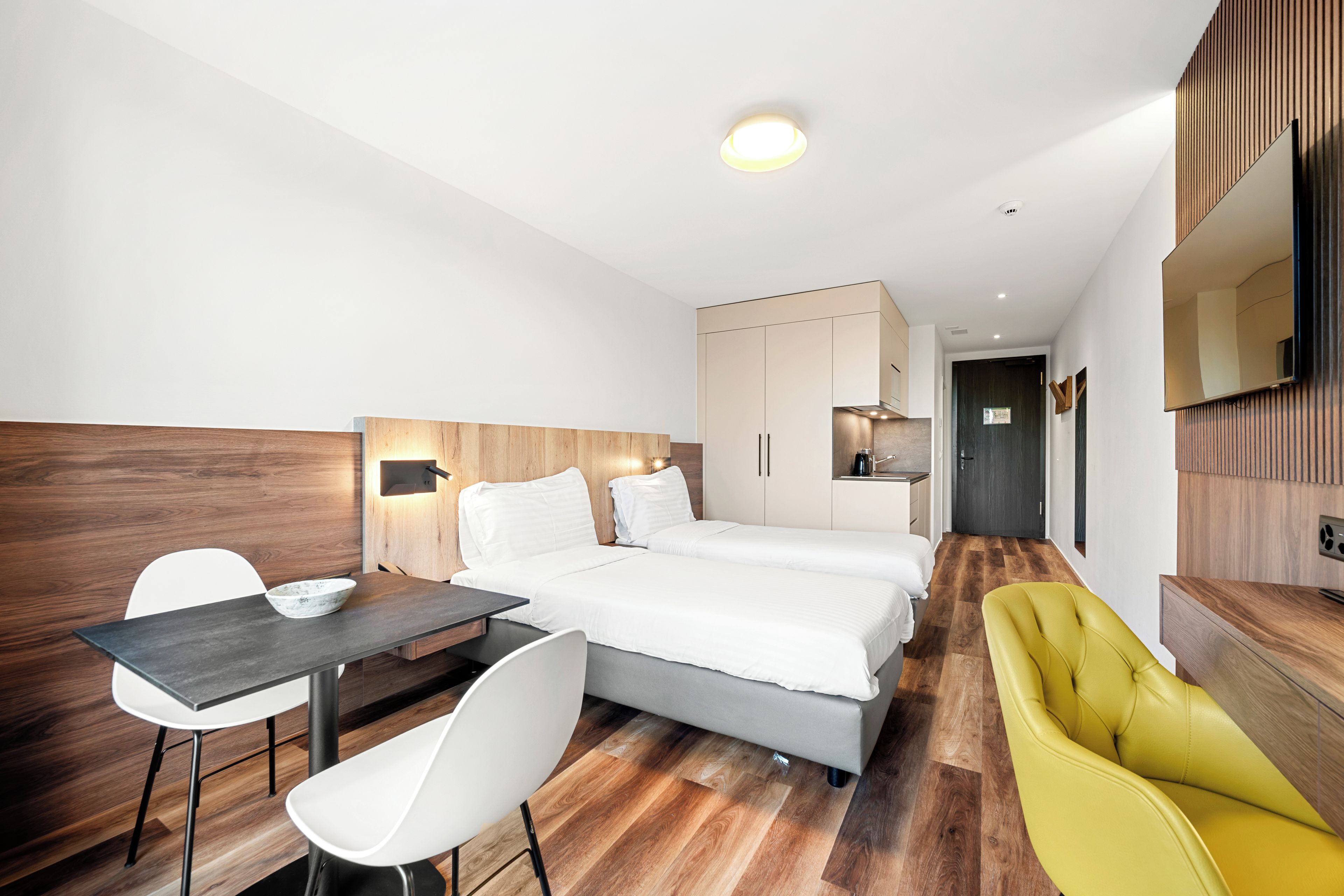 A modern hotel room with a bed, a desk, a chair, and a sofa.