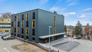 Een modern gebouw met een plat dak, meerdere ramen en een parkeerplaats ervoor.
