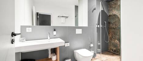 A modern bathroom with a white sink, a toilet, and a shower area.