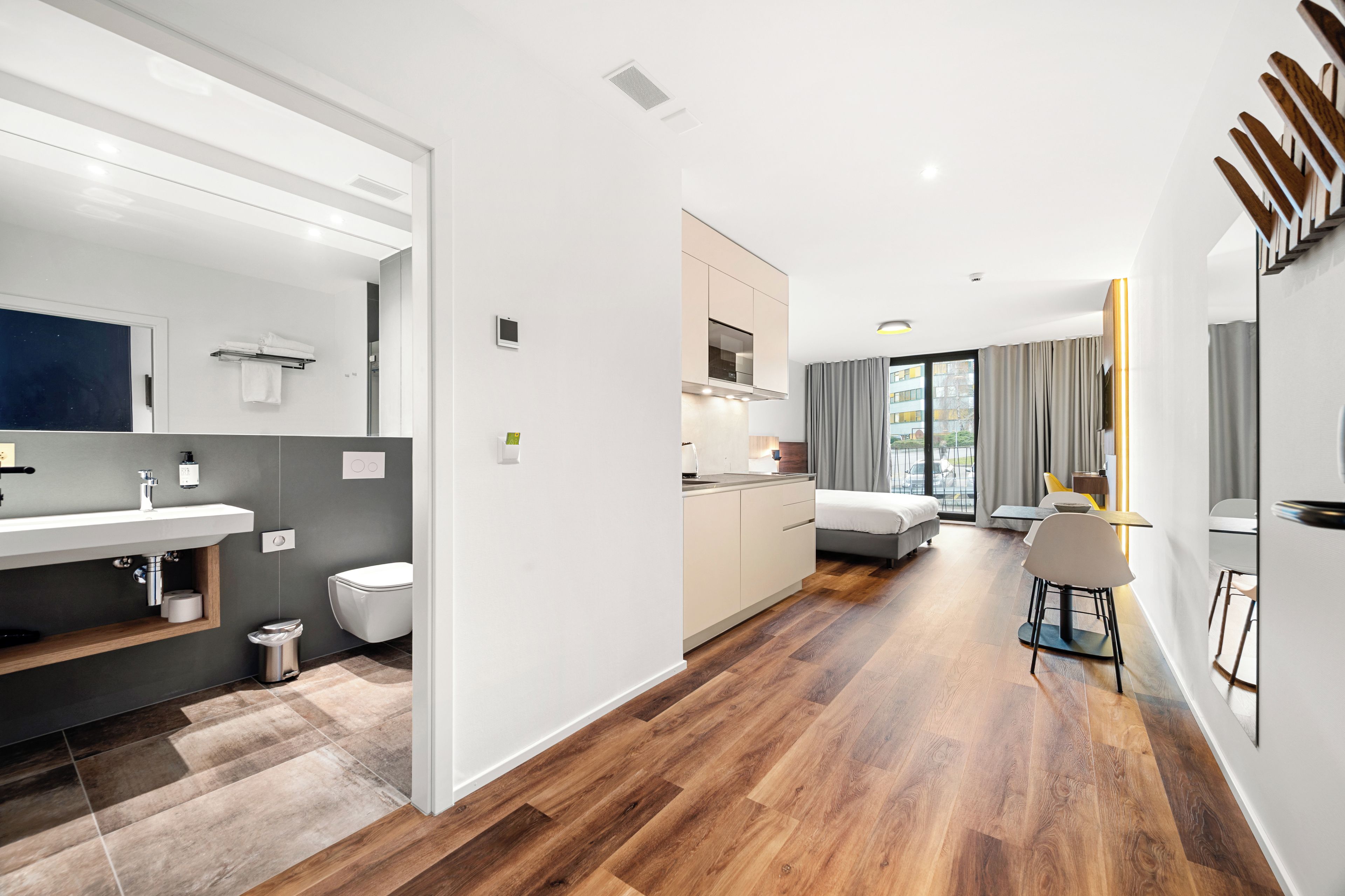 Ein modernes Hotelzimmer mit Bad, Küchenzeile und Blick auf die Stadt.