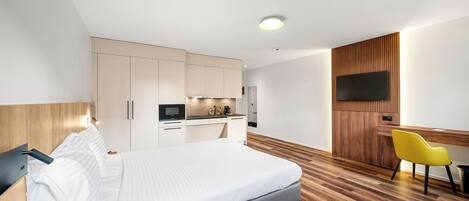 Una habitación de hotel moderna con una cama, un escritorio, un televisor y una kitchenette.