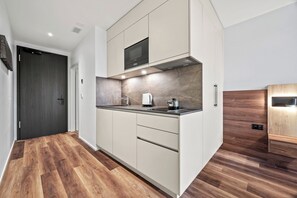 Een moderne keuken met een donker houten deur, witte kasten, een ingebouwde magnetron en een houten aanrecht.