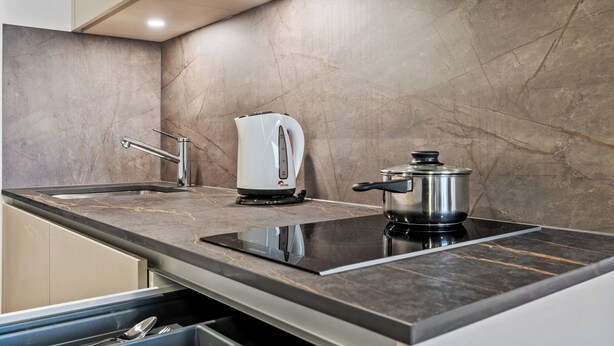 Een moderne keuken met een strak zwart aanrecht, een geïntegreerde inductiekookplaat, een waterkoker en een pan.