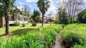 Een woonhuis met een verzorgde tuin, een kleine beek en diverse bomen en struiken.