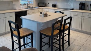 Moderni keittiö, jossa on valkoiset kaapit, keskellä sijaitseva saareke baarituoleineen, sisäänrakennettu mikroaaltouuni ja astianpesukone.
