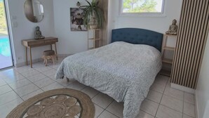 Une chambre à coucher comprenant un lit, une table de chevet, un luminaire suspendu, une fenêtre et une porte.