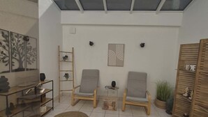 Une pièce baignée de lumière naturelle, avec une lucarne, deux chaises, une petite table et une bibliothèque.