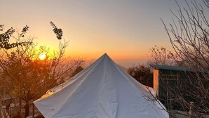 Una carpa blanca de techo cónico, rodeada por una barrera de cuerda, con el atardecer de fondo.