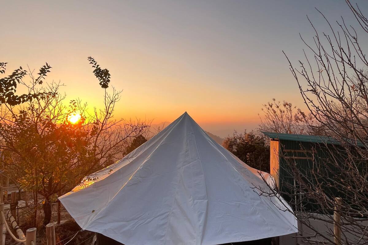 A white tent with a conical roof, surrounded by a rope barrier, set against a sunset backdrop.