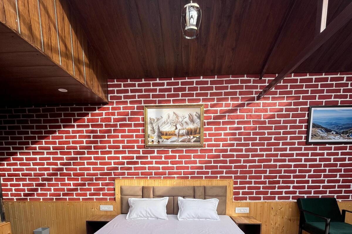 A bedroom with a brick-patterned wall, a bed with a quilt, a wooden headboard, a hanging light fixture, and a framed picture.