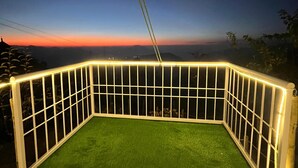 Un espacio exterior cercado con césped artificial, rodeado por una barandilla blanca con luces, con vistas a un atardecer.