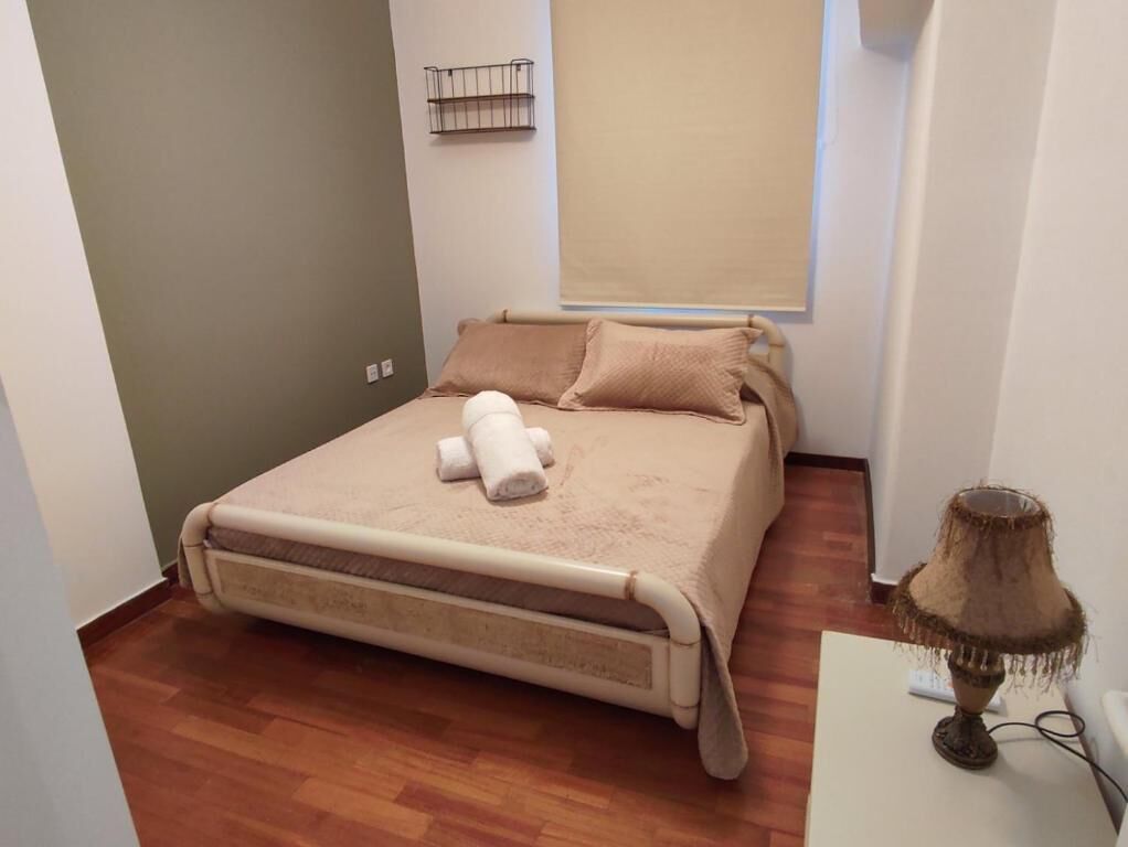 A small, neatly arranged bedroom with a bed, a bedside lamp, and a window with a blind.