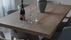 A dining area with a wooden table, grey chairs, a bottle of wine, and a vase.