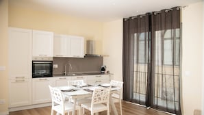 Une cuisine moderne avec des meubles blancs, une table à manger avec des chaises et une grande fenêtre agrémentée de rideaux.