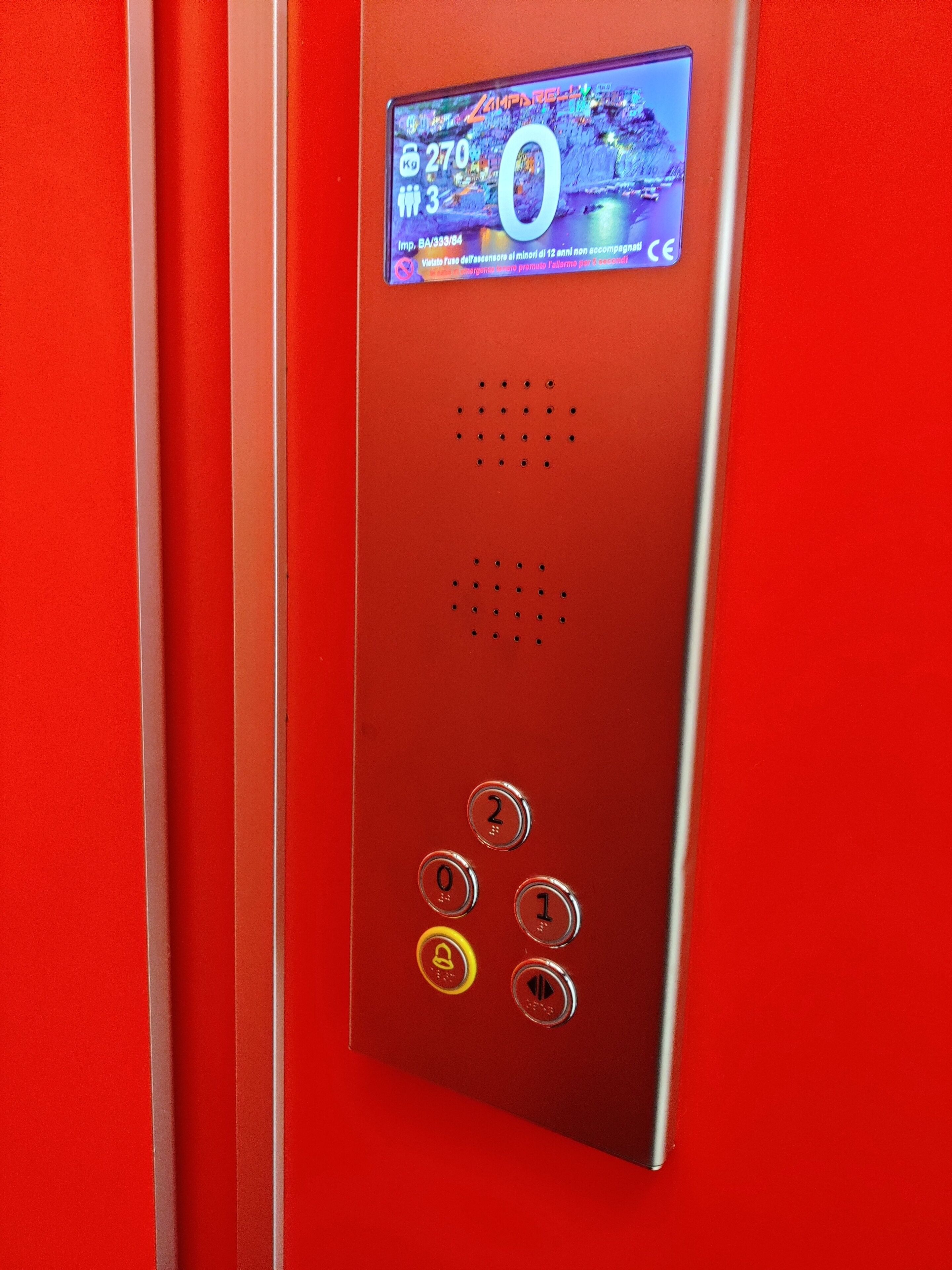 En röd manöverpanel för hissen med en digital display, knappar och ett högtalargaller.