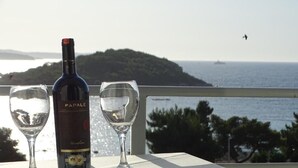 A bottle of wine and two glasses on a table with a view of the sea and a distant island.