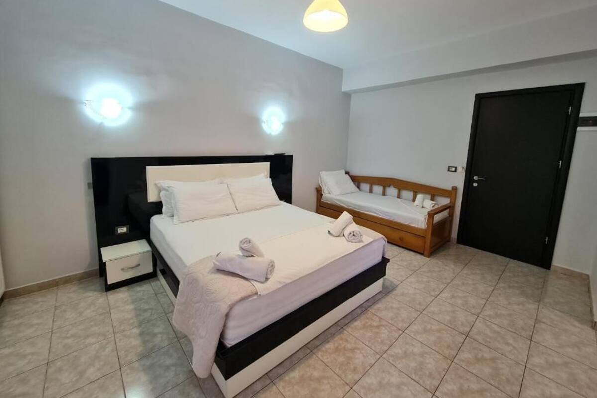 A bedroom with a large bed, a bedside table, a wooden bench, and a door.