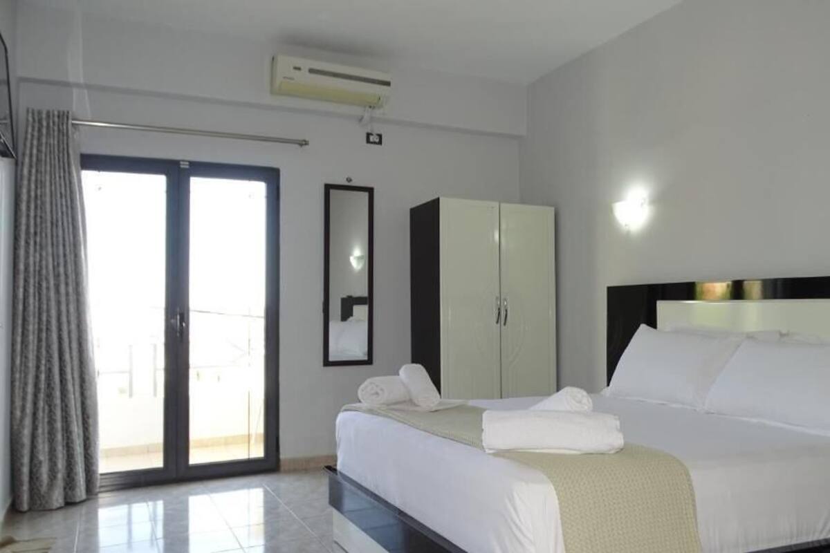 A hotel room with a bed, a wardrobe, a mirror, and a sliding glass door to the outside.