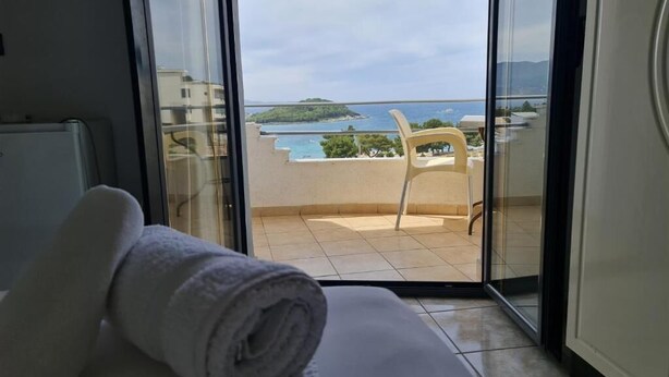 A hotel room with a large sliding glass door leading to a balcony with a view of the sea and a small island.