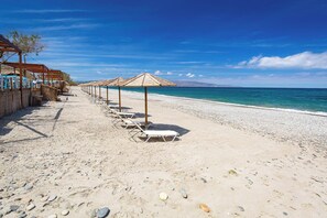 A beach with rows of sun loungers and umbrellas, a pebble beach, and a clear view of the sea.