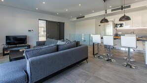 A modern living room with a grey sofa, a flat-screen TV, and a dining area with bar stools. - Menta Villa - Two Bedroom Villa, Sleeps 4 (Tavronitis)