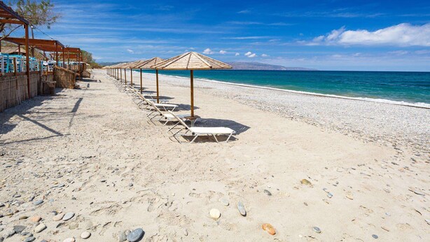 A beach with rows of sun loungers and umbrellas, a pebble beach, and a clear view of the sea. - Menta Villa - Two Bedroom Villa, Sleeps 4 (Tavronitis)