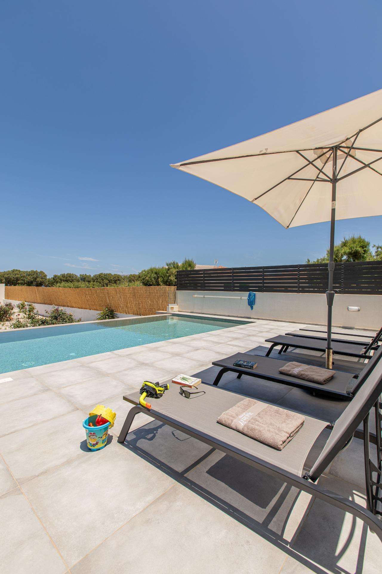 Zona de piscina con sillones de descanso, una sombrilla y área de juegos para niños.