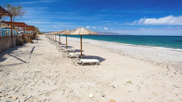 A beach with rows of sun loungers and umbrellas, a pebble beach, and a clear view of the sea.