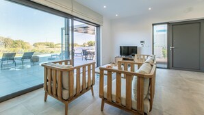 A modern living room with large glass doors leading to an outdoor patio, a flat-screen TV, and a sliding door to a balcony.
