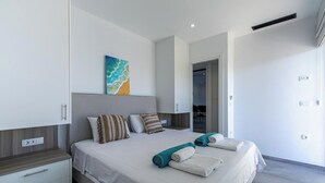 A modern bedroom with a large bed, a painting, and a view of the dining area.