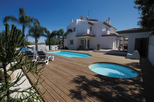 A pool area with a wooden deck, a hot tub, and lounge chairs.