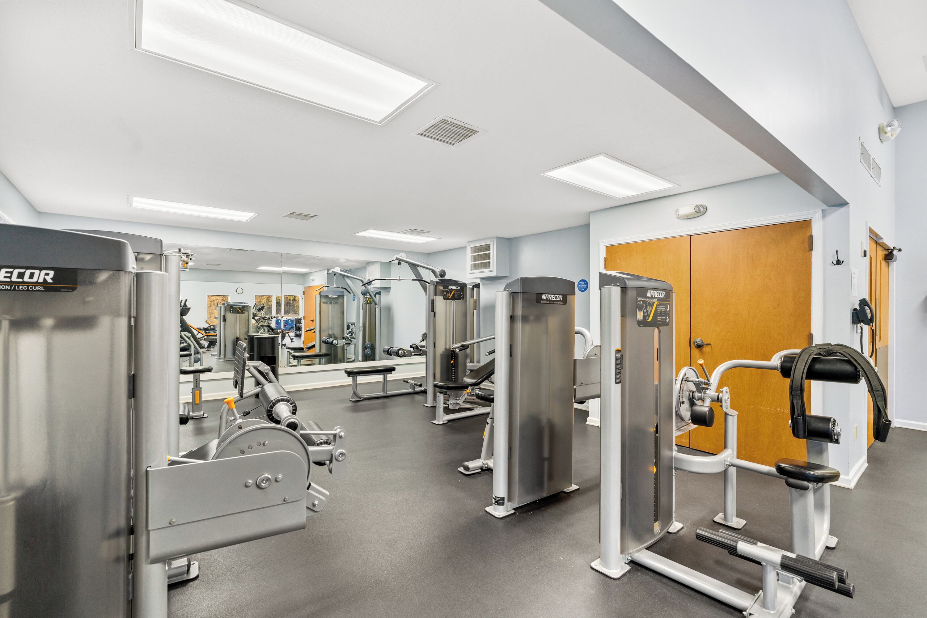 Un gimnasio con diferentes máquinas de ejercicio, un espejo y una puerta de madera.