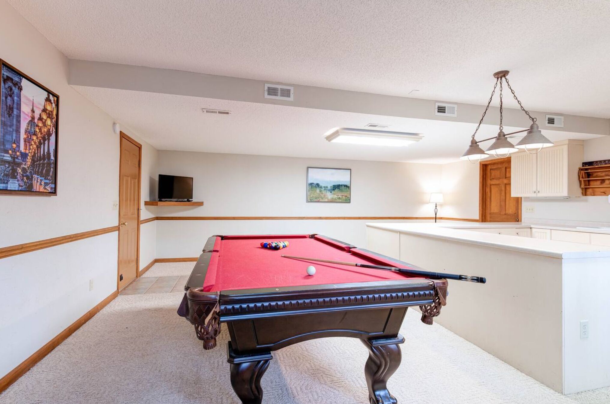 A pool table in a room with a wooden door, a television, and a framed picture on the wall.