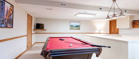 A pool table in a room with a wooden door, a television, and a framed picture on the wall.