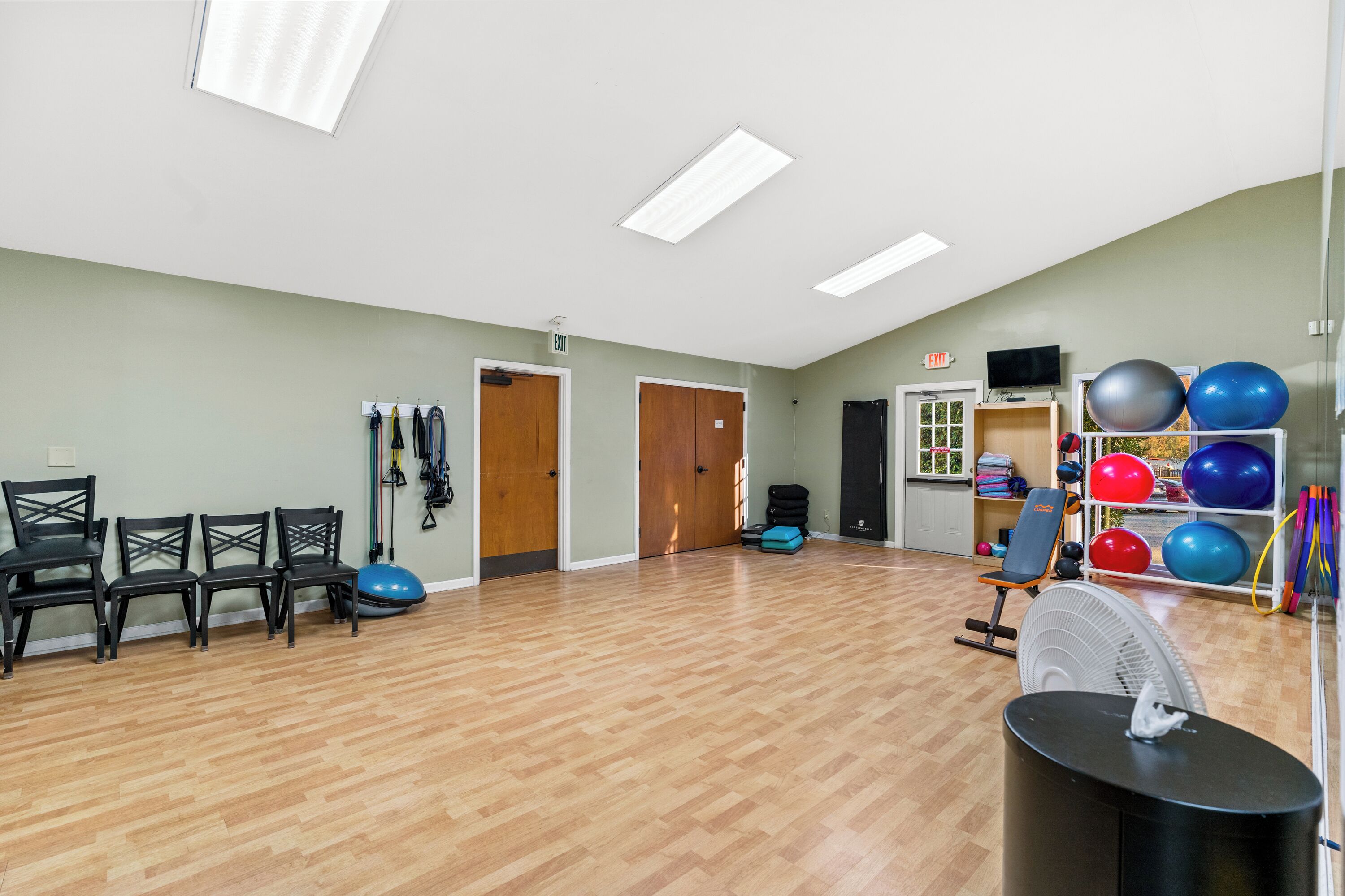 A spacious room with wooden flooring, exercise equipment, and a fan.