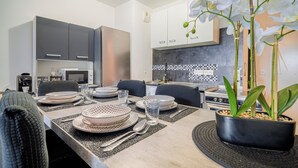 Une cuisine moderne avec des meubles gris, un four à micro-ondes et une cuisinière. On y trouve une table à manger mise avec des assiettes, des verres et des couverts.