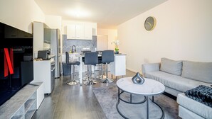Un salon moderne avec un canapé gris, une table basse ronde et un coin repas comprenant une table blanche et quatre chaises.