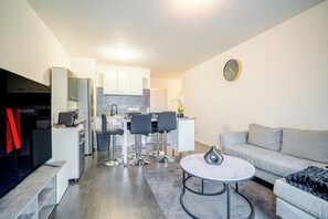 A modern living room with a grey sofa, a round coffee table, and a dining area with a white table and four chairs. - Appart Standing (Trappes)