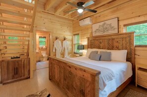 A wooden cabin bedroom with a bed, bedside tables, a ceiling fan, and a window.