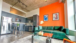 Una sala de estar moderna con un sofá verde, una mesa de centro de vidrio y una cocina al fondo.