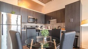 Una cocina moderna con armarios oscuros, electrodomésticos de acero inoxidable y una mesa de vidrio con cuatro sillas.